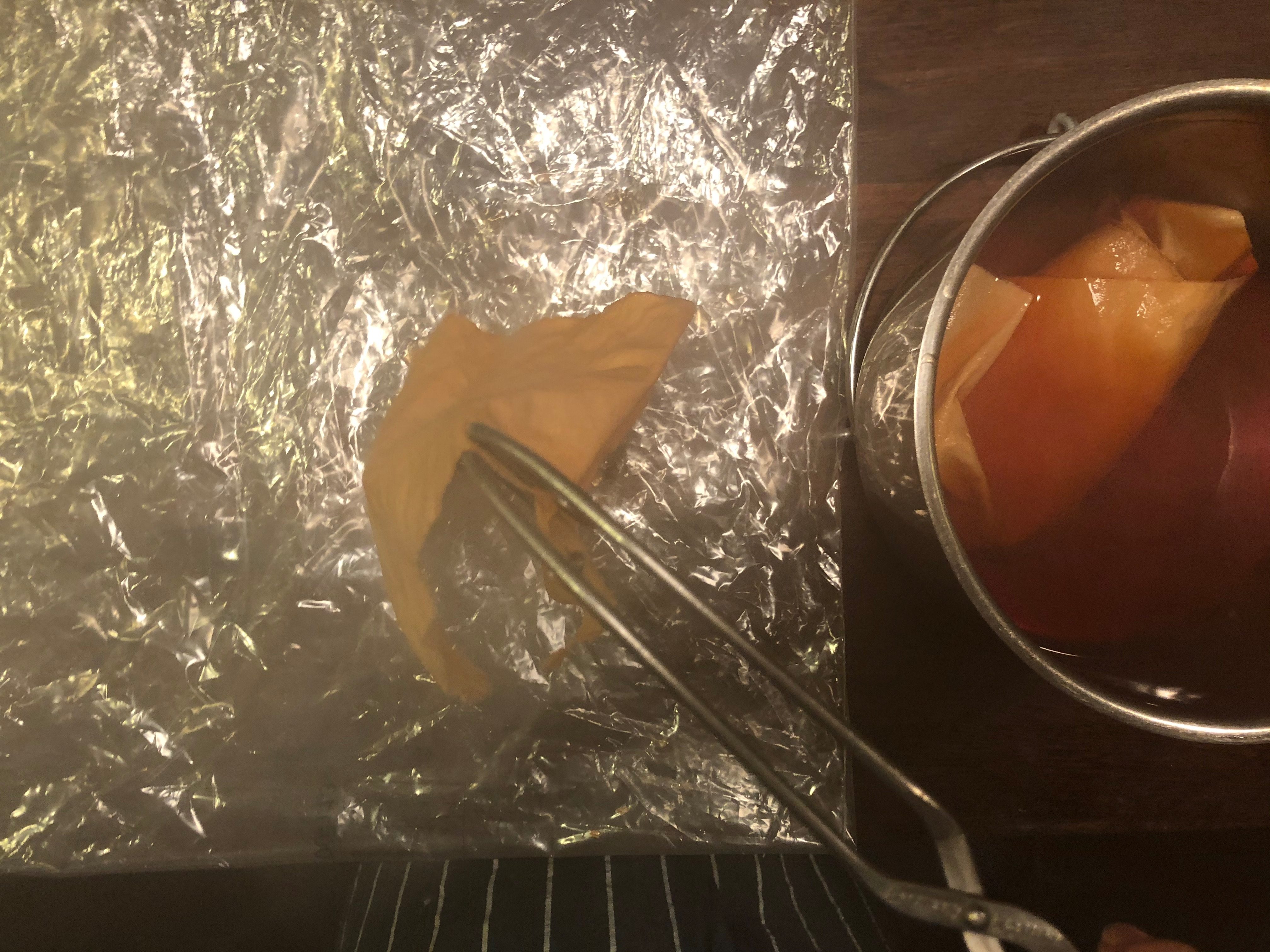 Tongs removing fabric from saucepan and hovering over plastic sheet.